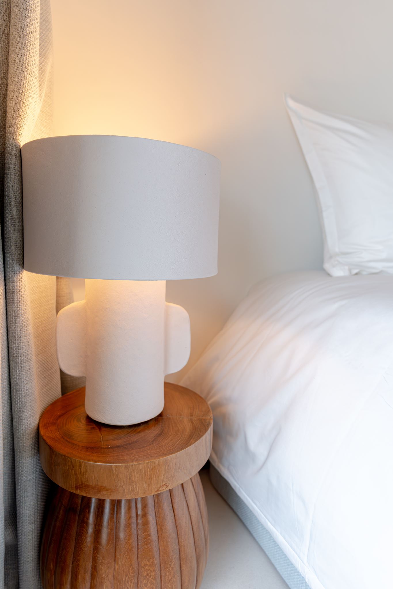 Lampe en céramique sur guéridon en bois, chevet d'une chambre épurée